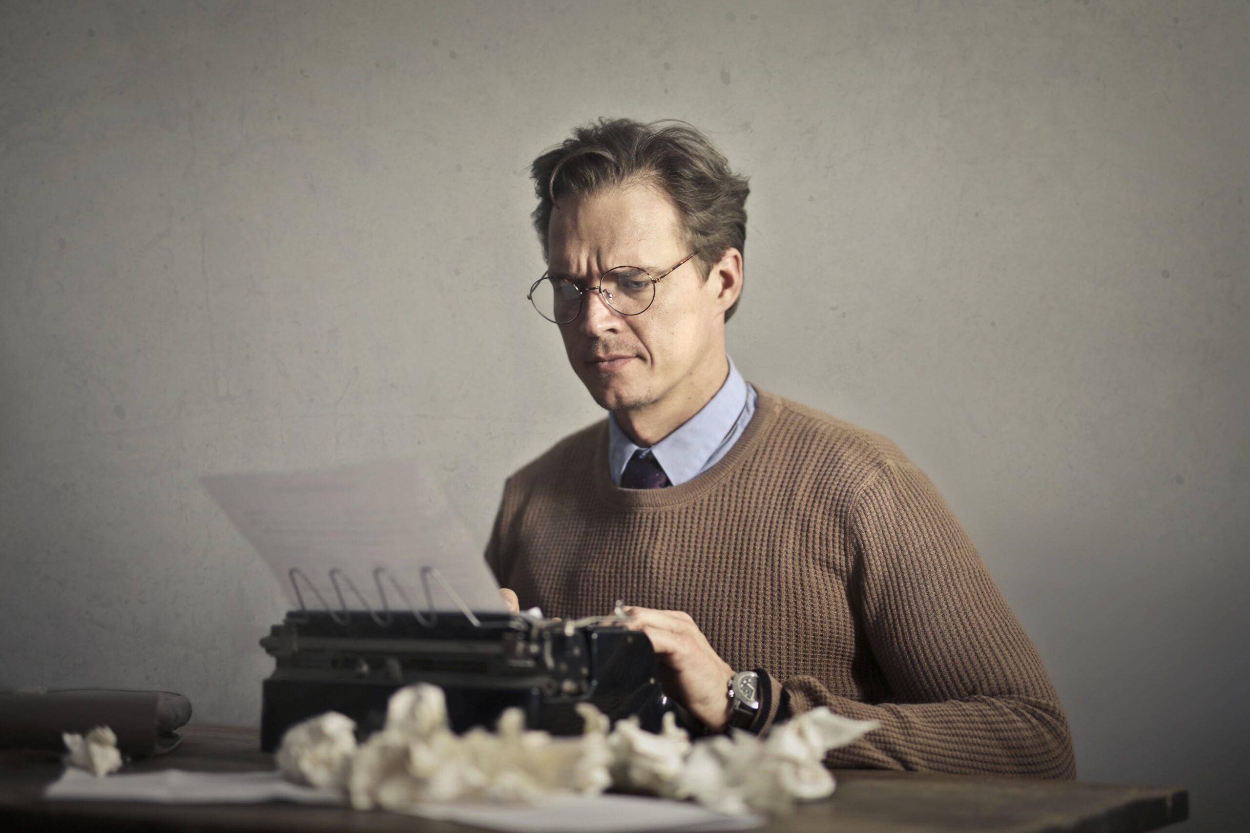 A thoughtful writer using a typewriter surrounded by crumpled paper, embodying vintage creativity.